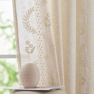 Beige curtain with floral patterns beside a textured vase.