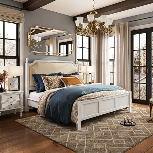 Elegant bedroom with white bed, blue and gold bedding, and large windows.