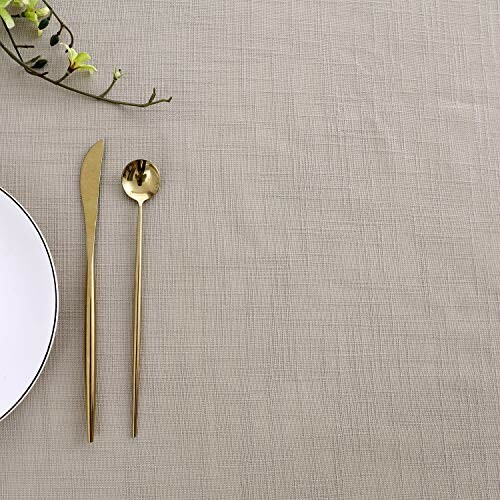 Elegant table setting with gold cutlery and a plate on a textured tablecloth.