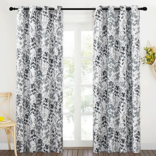 Black and white floral curtains on a window with a chair and plant decor.