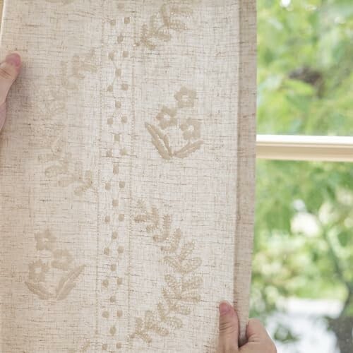 Hands holding a piece of embroidered fabric near a window.