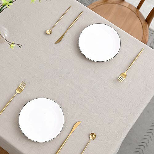 Minimalist dining table with plates, gold cutlery, and neutral tablecloth.