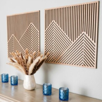 Geometric wooden wall art above a table with a vase of pampas grass and blue candles.