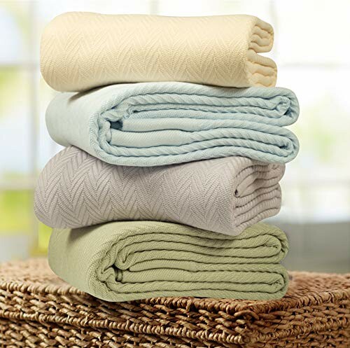 Stack of four woven blankets in neutral colors on a wicker surface.
