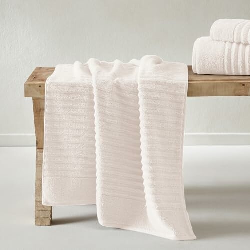 White towels draped on a wooden bench with stacked towels beside.