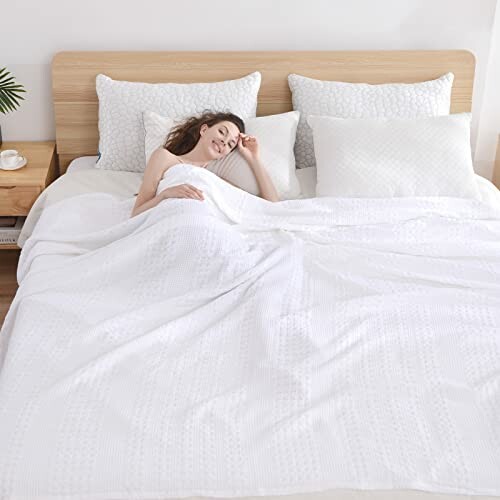 Woman sleeping peacefully in white bedding with wooden headboard and pillows.